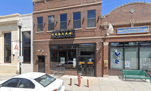 A brick building with a sign reading "Riptide," next to another storefront, on a city street.