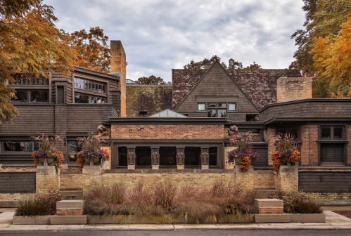 A modern architectural building with a mix of brick and wood, surrounded by colorful plants and trees in autumn.