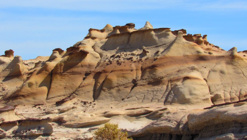A rugged, sandy rock formation with unique shapes and textures under a clear blue sky.