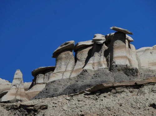 Rock formations with distinct cap-like structures against a clear blue sky.
