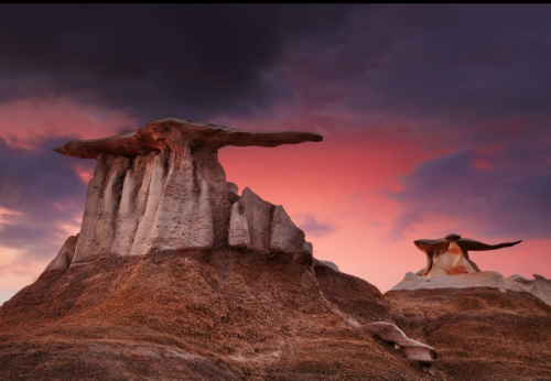 Two unique rock formations against a colorful sunset sky, with dramatic clouds enhancing the landscape's beauty.