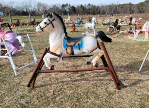 A vintage rocking horse on a grassy field, surrounded by other colorful toy horses in the background.