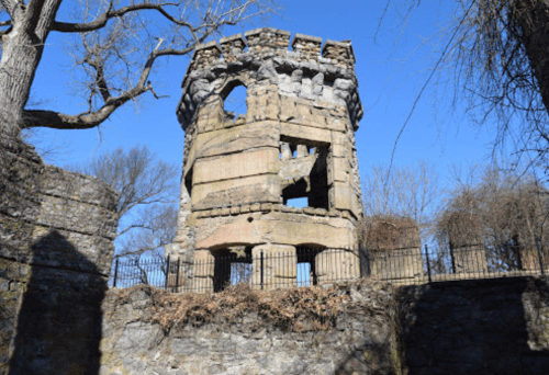 Ruins of a stone tower with broken windows, surrounded by trees and a clear blue sky.