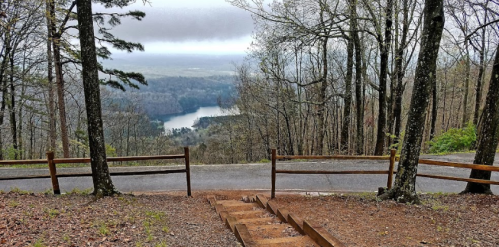 A scenic view from a forested overlook, featuring a winding river and misty mountains in the distance.