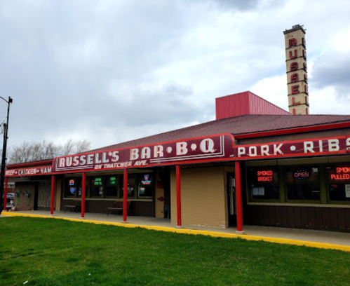 Exterior of Russell's Bar-B-Q, featuring a red sign and a grassy area, under a cloudy sky.