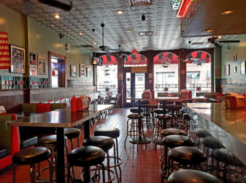 A cozy restaurant interior with colorful seating, bar stools, and large windows, featuring a vintage decor style.