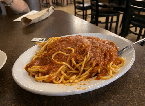 A plate of spaghetti topped with marinara sauce, served on a brown table in a casual dining setting.