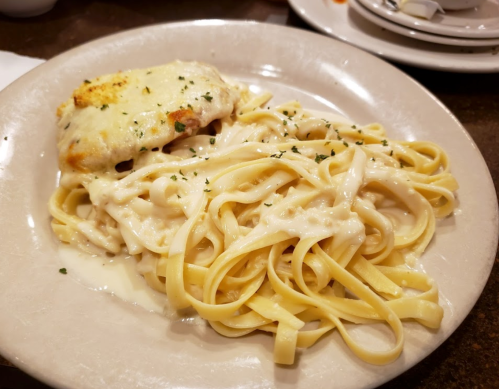 A plate of fettuccine pasta topped with creamy sauce and a piece of baked fish, garnished with herbs.