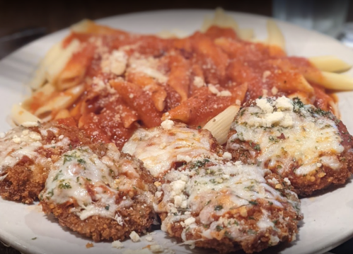 A plate of pasta with marinara sauce and four cheesy, breaded chicken cutlets.