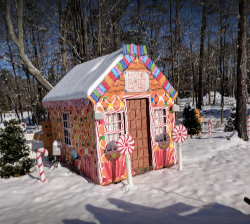 A whimsical gingerbread house decorated with candy, surrounded by snow and trees, with a sign reading "Home Sweet Home."