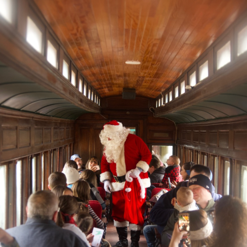Santa Claus interacts with children on a festive train, surrounded by families enjoying the holiday spirit.