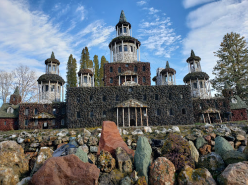 A unique stone castle with multiple towers, surrounded by colorful rocks and trees under a blue sky.