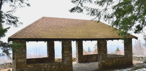 A stone pavilion with a wooden roof, surrounded by trees and overlooking a misty landscape.