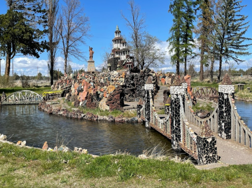 A scenic park featuring a rocky landscape, a small bridge, and a unique tower structure against a blue sky.