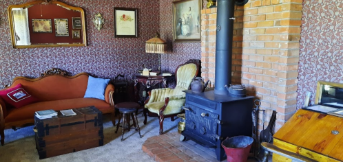 Cozy vintage living room with patterned wallpaper, a brick fireplace, and antique furniture.