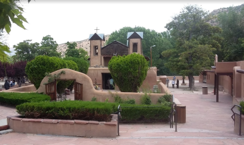 A scenic view of a southwestern-style building surrounded by greenery and pathways, with people in the background.