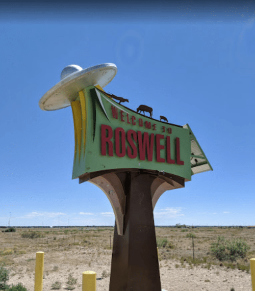 A colorful "Welcome to Roswell" sign featuring a UFO against a clear blue sky and desert landscape.