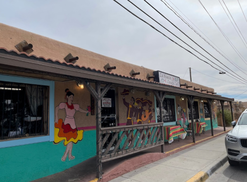 Colorful restaurant exterior with murals, featuring a dancer and festive decorations, under a cloudy sky.