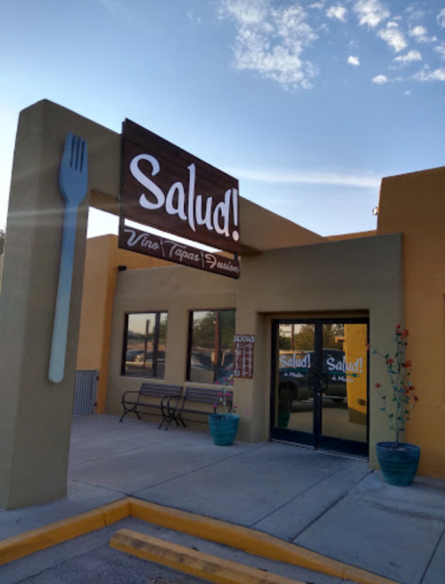 Exterior of a restaurant named "Salud!" featuring a large fork sign and colorful planters. Clear blue sky in the background.