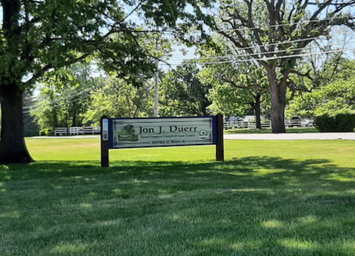Sign for Jon J. Duerr Funeral Home, surrounded by green grass and trees, with a clear blue sky in the background.