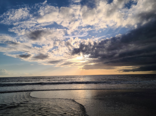 A serene beach scene at sunset, with clouds reflecting golden light over calm waves and a tranquil shoreline.