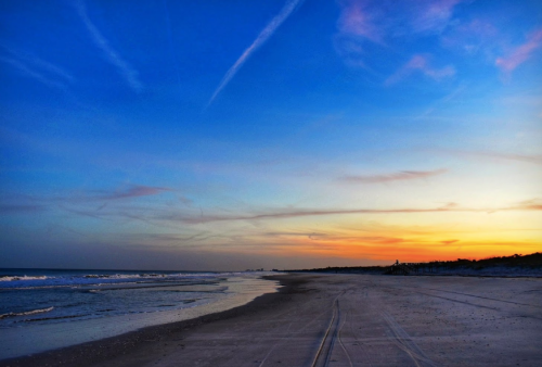 A serene beach at sunset, with soft waves and a colorful sky transitioning from blue to orange.