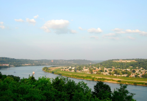 A scenic view of a river winding through green hills and a small town under a clear blue sky.