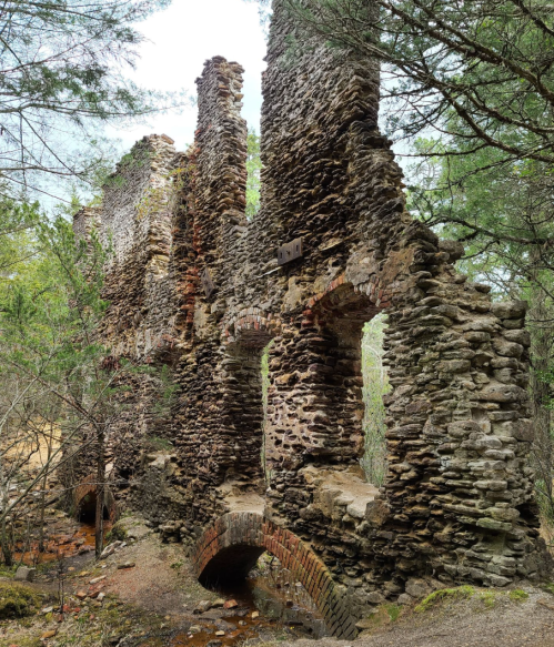 Ruins of a stone structure surrounded by trees, with partially collapsed walls and arched openings.