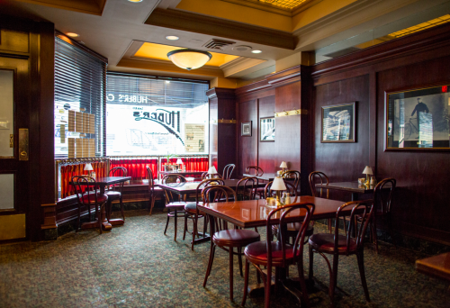 Cozy restaurant interior with wooden tables, chairs, and large windows, featuring warm lighting and a classic decor.