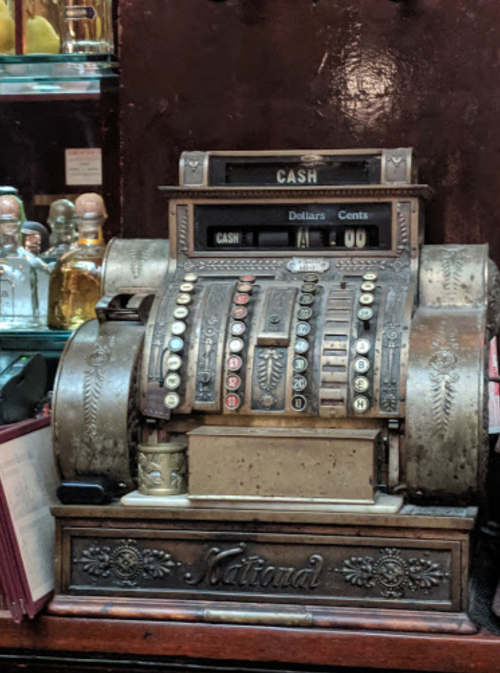 An antique cash register with ornate details, displaying "CASH" and various buttons for dollars and cents.