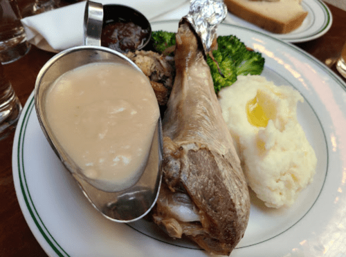 A plate featuring a fish fillet, mashed potatoes with gravy, broccoli, and a side of sauce.