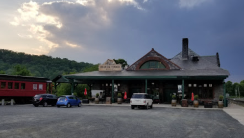 Historic train station with a green facade, parked cars, and a cloudy sky in the background.