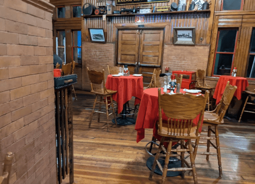 Cozy restaurant interior with wooden floors, red tablecloths, and rustic decor. Empty tables set for dining.