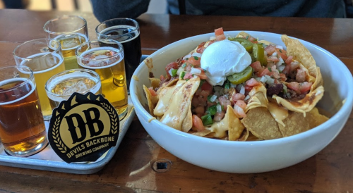 A bowl of nachos topped with cheese, tomatoes, jalapeños, and a dollop of sour cream, alongside a flight of beers.