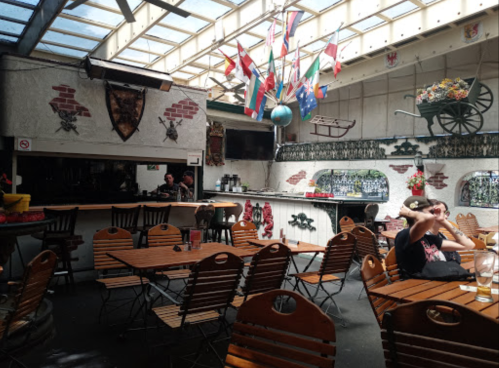 A spacious indoor restaurant with wooden tables, flags hanging from the ceiling, and a bar area in the background.