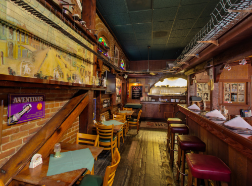 Cozy restaurant interior with wooden beams, bar area, and tables, featuring warm lighting and rustic decor.