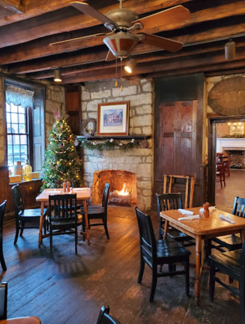 Cozy restaurant interior with wooden tables, a fireplace, and a Christmas tree, creating a warm, inviting atmosphere.