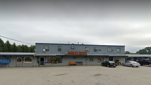 A two-story blue building with a sign reading "Rusty Can," surrounded by a parking lot and trees.