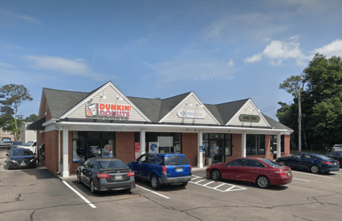 A brick building with a Dunkin' Donuts, XpressMart, and a bank, surrounded by parked cars and trees.