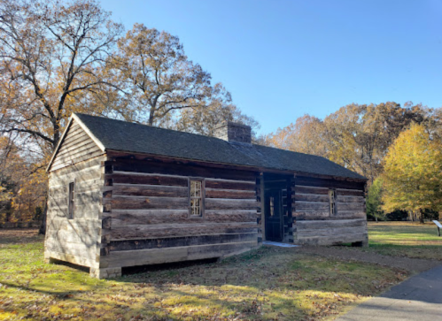 A rustic log cabin surrounded by trees, set against a clear blue sky in a serene outdoor setting.