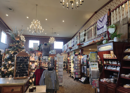 A cozy gift shop with chandeliers, decorated for the holidays, featuring shelves of products and a Christmas tree.