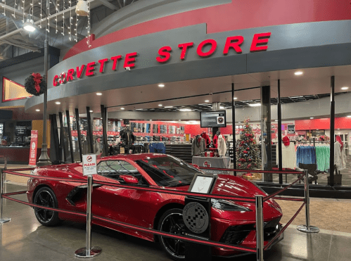 A red Corvette parked in front of the Corvette Store, featuring festive decorations and merchandise displays.