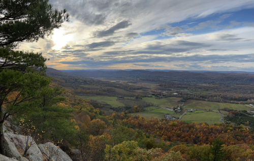 A panoramic view of rolling hills and valleys, showcasing vibrant autumn foliage under a cloudy sky.