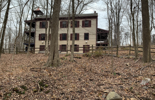 A large wooden building surrounded by bare trees and fallen leaves, set in a wooded area.