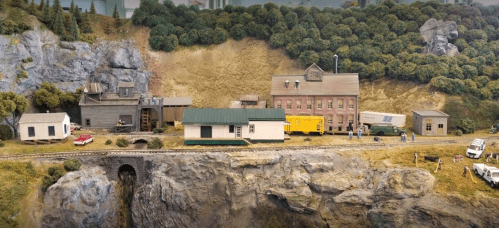 A detailed model train scene featuring buildings, vehicles, and a rocky landscape.