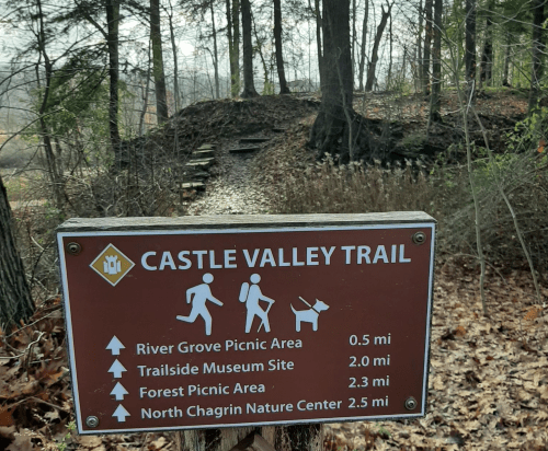 Sign for Castle Valley Trail with directions to picnic areas and nature center, surrounded by trees and a misty landscape.