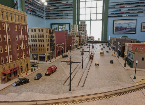 A detailed model city scene with buildings, streets, and vintage cars, showcasing a miniature urban landscape.