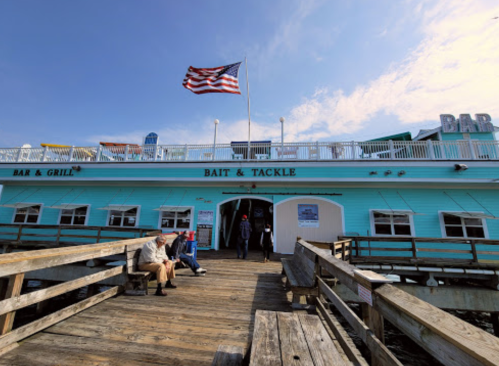 A turquoise building with a sign reading "Bait & Tackle" and an American flag, located on a wooden pier.
