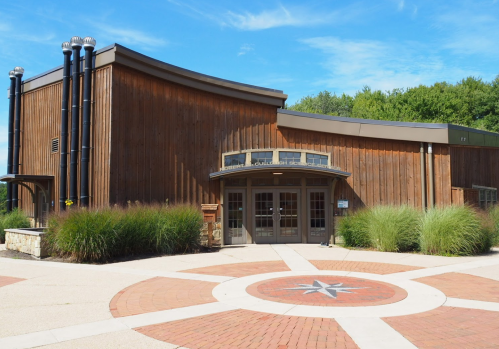 A modern wooden building with large windows, surrounded by greenery and a circular brick pathway.