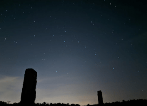 Two stone pillars silhouetted against a starry night sky with faint clouds and a soft glow on the horizon.